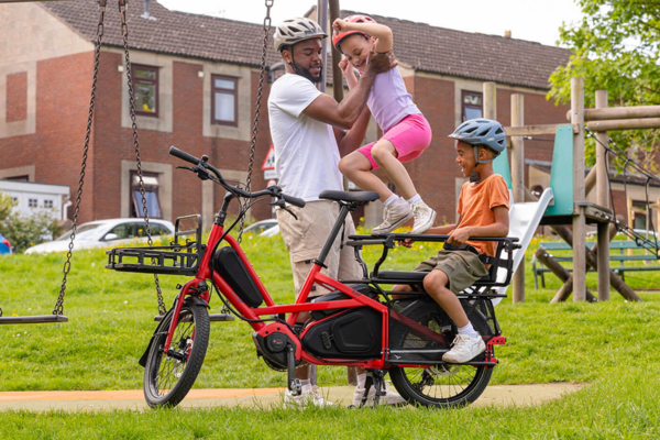 Famille avec un vélo longtail Tern Quick Haul Long rouge sur une aire de jeux
